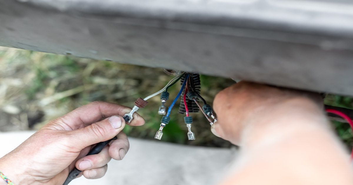 A person holds multiple wires in their hands that stem from the bottom edge of a vehicle in front of them.