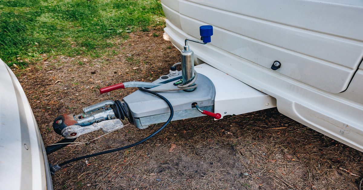 The connecting joint between a white vehicle and a trailer with various cables connecting the two ends.